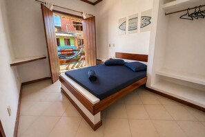 A bedroom with a bed, a wooden headboard, a nightstand, a wardrobe, and a view of a colorful building outside. - Nossa Casa Itacaré (Itacaré)