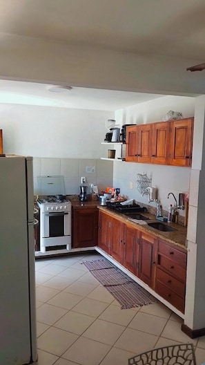A compact kitchen with a stove, sink, and wooden cabinets. - Nossa Casa Itacaré (Itacaré)