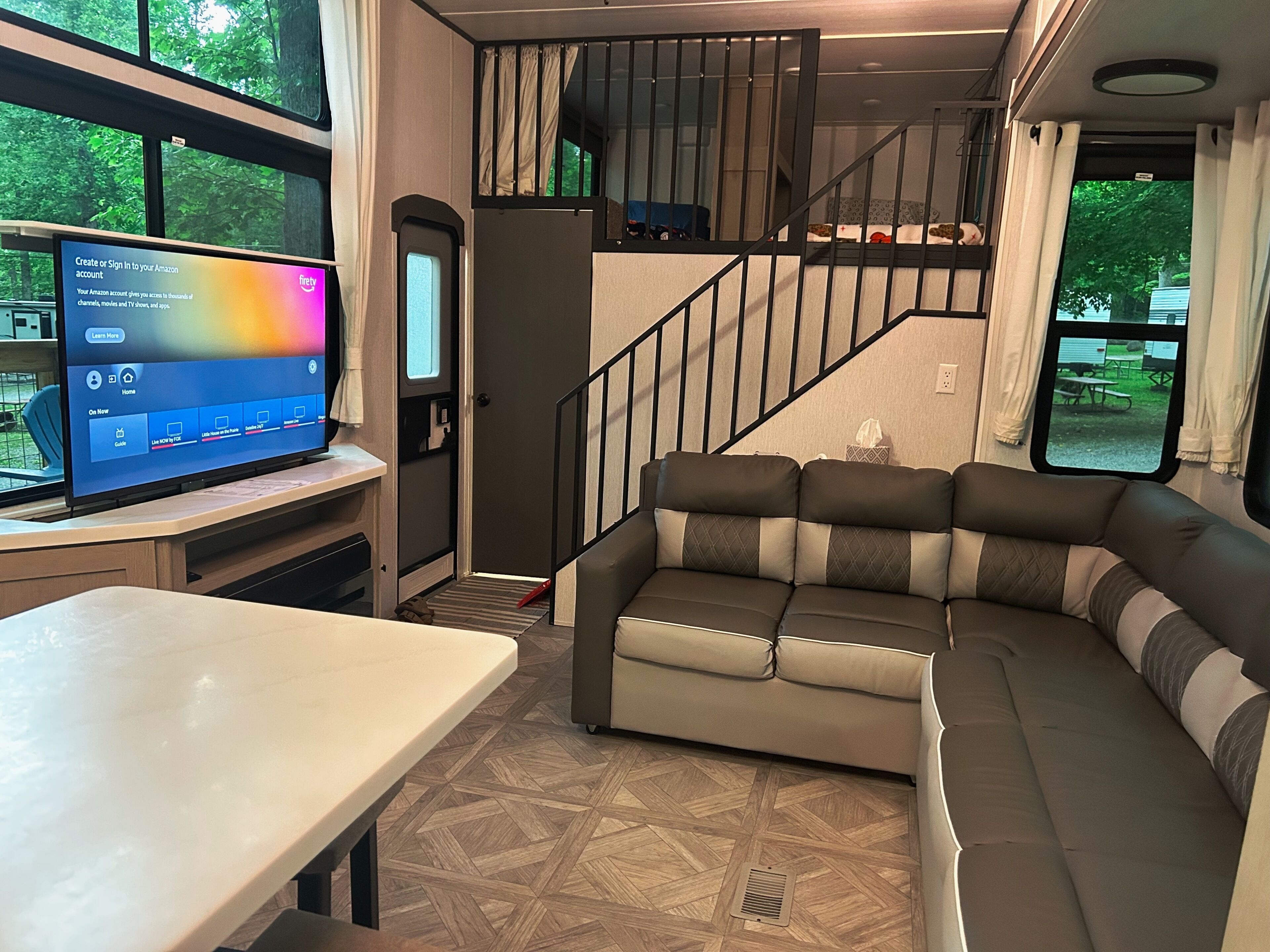 Un interior de autocaravana moderno con un sofá modular, un televisor de pantalla plana y una escalera que lleva a un nivel superior.