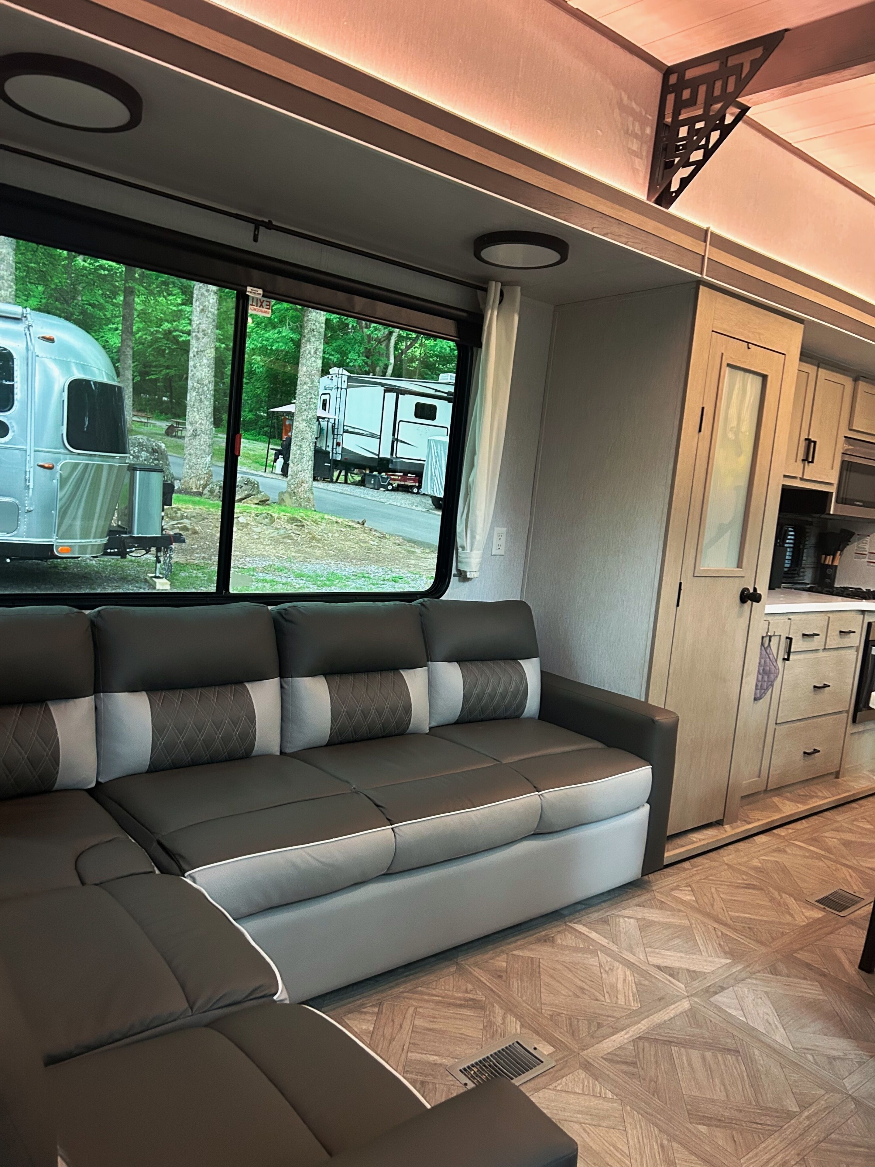Interior moderno de autocaravana con sofá modular, zona de cocina y vistas al exterior.
