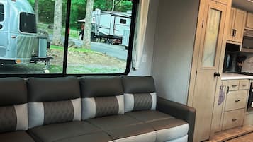 Interior moderno de autocaravana con sofá modular, zona de cocina y vistas al exterior.