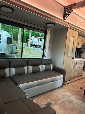 Ein modernes Wohnmobil-Interieur mit einer Eckcouch, einer Küchenzeile und Blick ins Freie.
