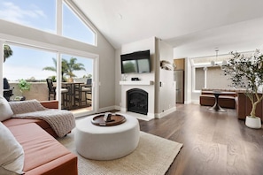 A spacious living room with a fireplace, a television mounted above it, and a large window overlooking a patio area.