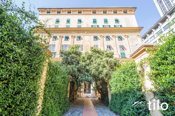 A building with a central entrance, surrounded by lush greenery, and a clear sky above. - Train Station| 3BR| A/C| City Center By Tilo (Genova)