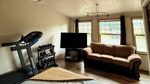 A room with a ceiling fan, a treadmill, a sofa, a TV, and large windows. - Spacious 4-bed in Eugene - Gated, Fenced Estate 10 min from Downtown/Wineries (Eugene)