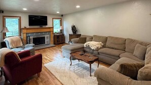 A living room with a fireplace, a sofa, a red armchair, and a wooden coffee table. - Spacious 4-bed in Eugene - Gated, Fenced Estate 10 min from Downtown/Wineries (Eugene)