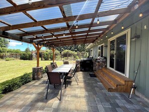 A covered patio with a table and chairs, a grill, and a fishing rod. - Spacious 4-bed in Eugene - Gated, Fenced Estate 10 min from Downtown/Wineries (Eugene)