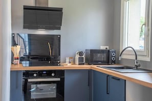 A compact kitchen with a microwave, toaster, oven, and a window providing natural light. - T2 moderne et chaleureux en centre-ville (Lorient)