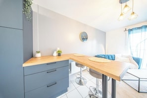 A modern kitchen with a wooden countertop, grey cabinets, a round clock, and a blue chair. - T2 moderne et chaleureux en centre-ville (Lorient)