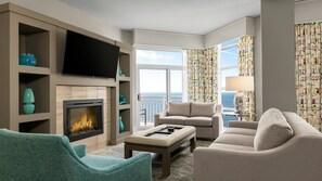 A hotel room with a fireplace, a television, a sofa, a chair, and a view of the sea.