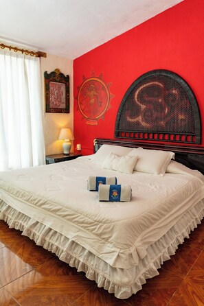 A neatly made bed with a ruffled bed skirt, a headboard with a circular design, a wall-mounted artwork, and a bedside table with a lamp.