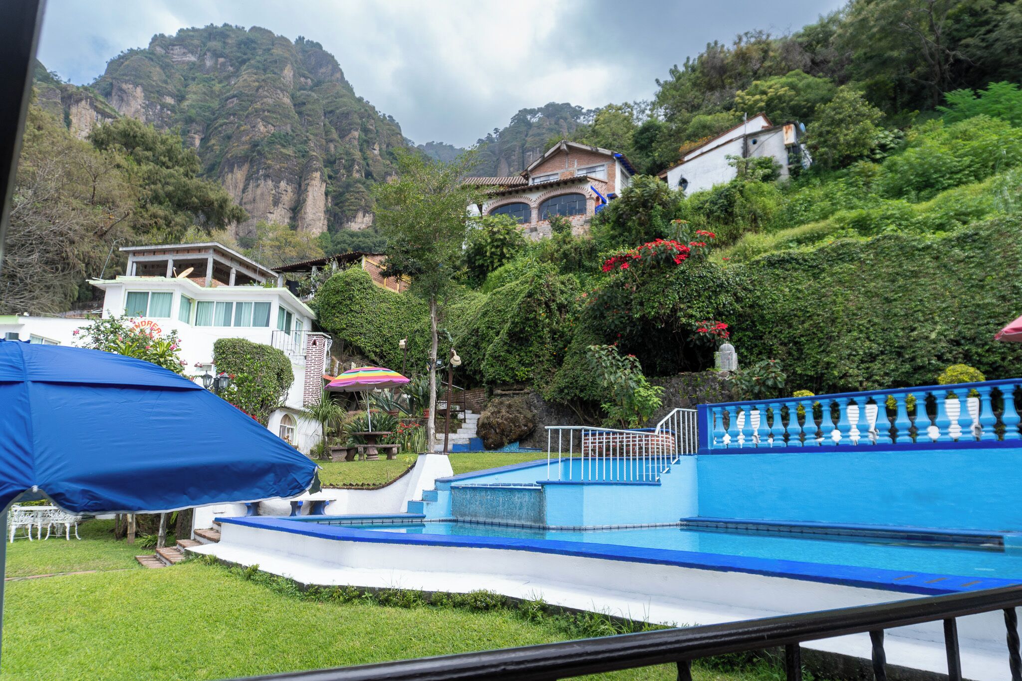 Una piscina con decoración azul y blanca, rodeada de exuberante vegetación y montañas al fondo.