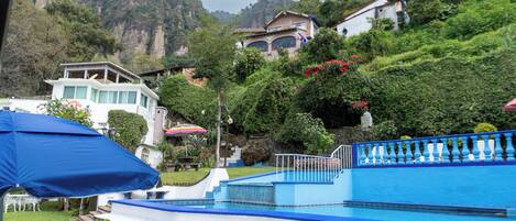A swimming pool with a blue and white color scheme, surrounded by lush greenery and a mountainous backdrop.