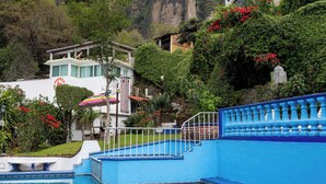 Piscina con borde azul, rodeada de vegetación exuberante y montañas al fondo.
