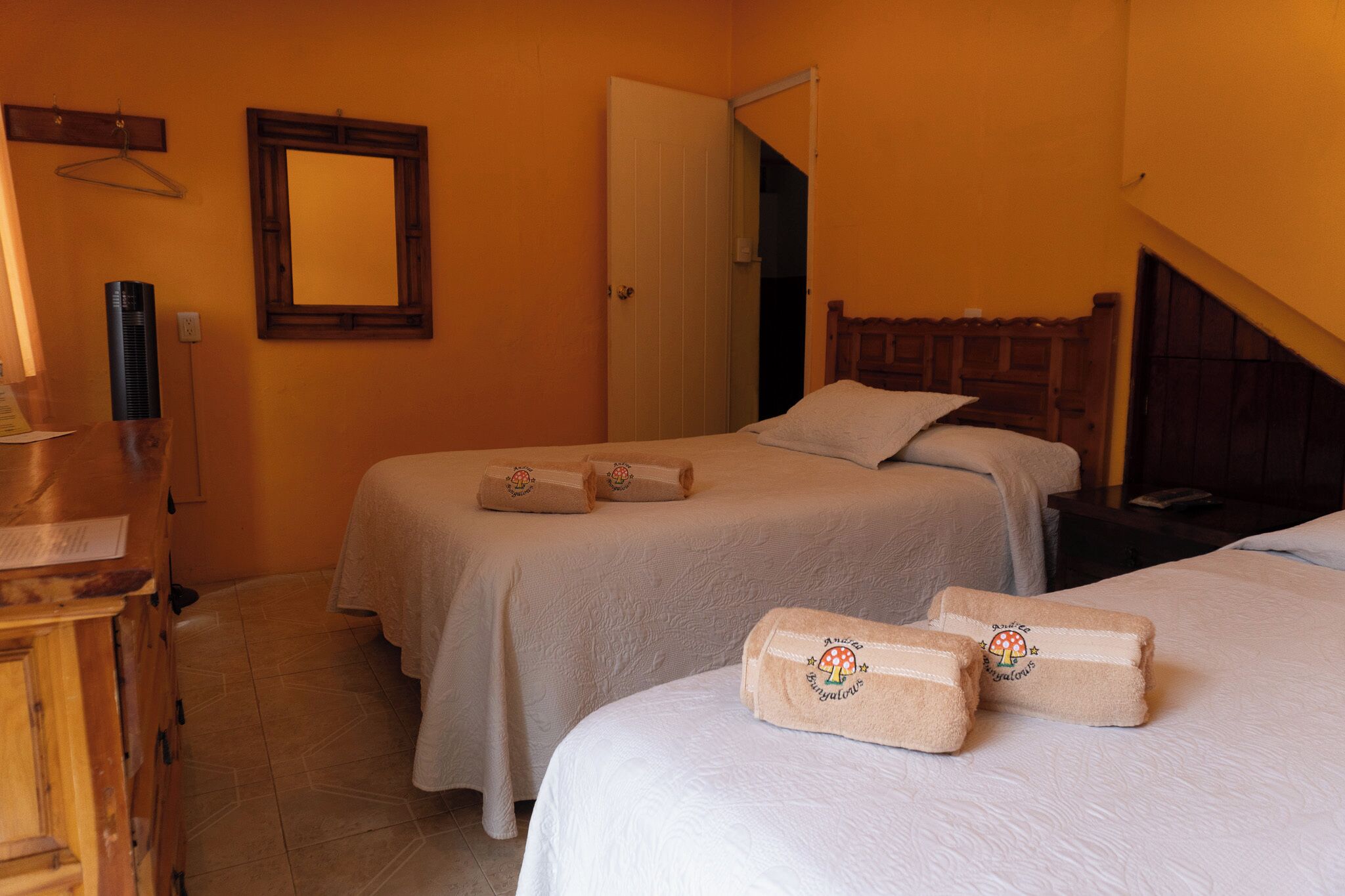 A hotel room with two beds, a wooden headboard, a mirror, a wooden dresser, and towels with a mushroom design.