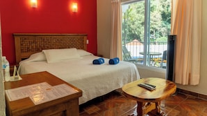 Una habitación de hotel con una cama, cabecera de madera, una ventana con cortinas, una mesita y una silla.