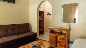 Una habitación con sofá, una pequeña mesa de madera, un armario, un espejo y un arco que da a un vestidor.