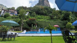 Un jardín con mobiliario exterior, una piscina y montañas al fondo.