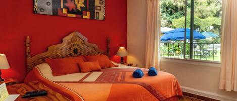 Habitación de hotel con cama, mesita de noche, lámpara, ventana con cortinas y vistas al exterior.