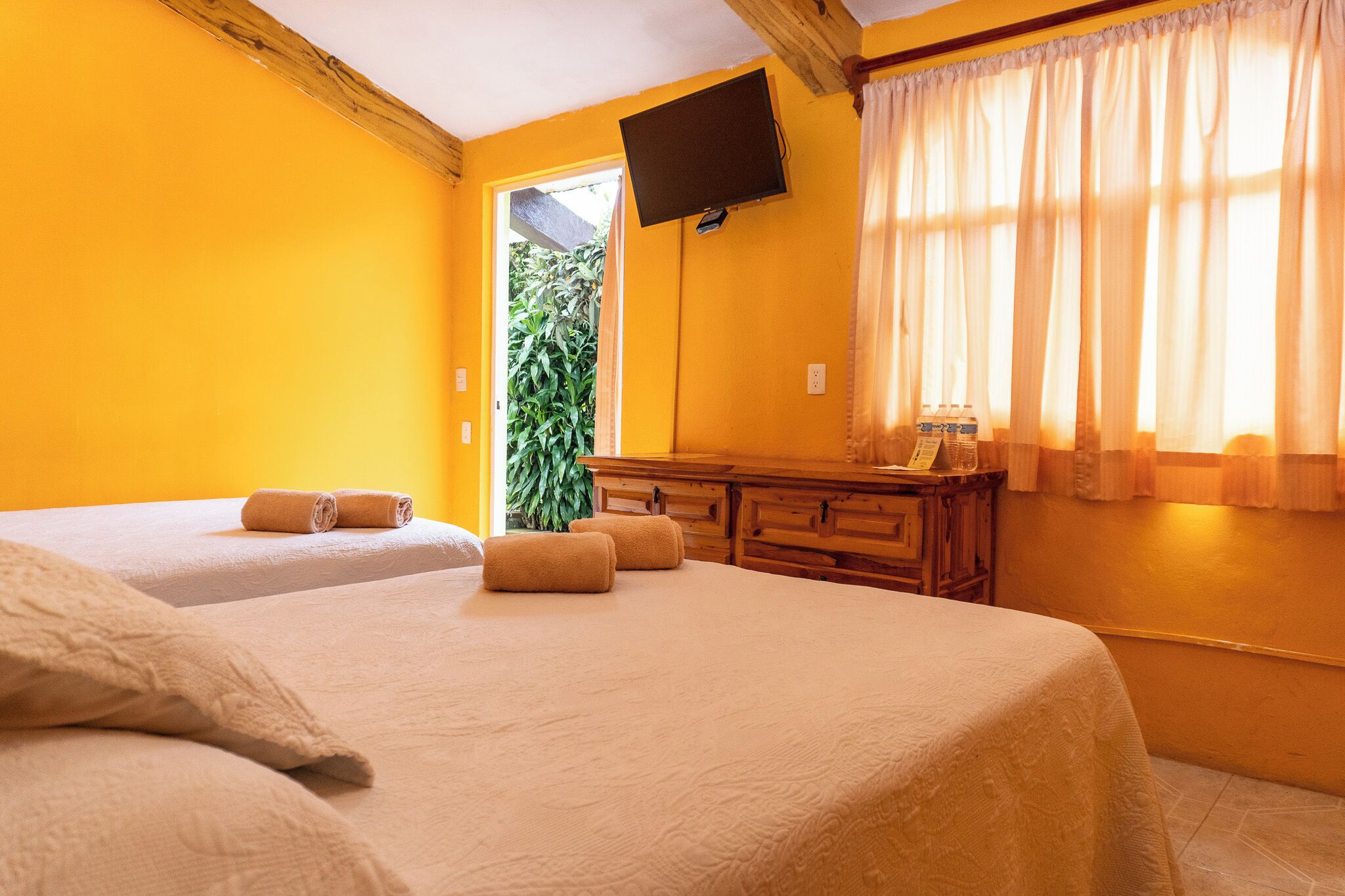 A hotel room with two beds, a wooden dresser, a flat-screen TV, and a window with curtains.