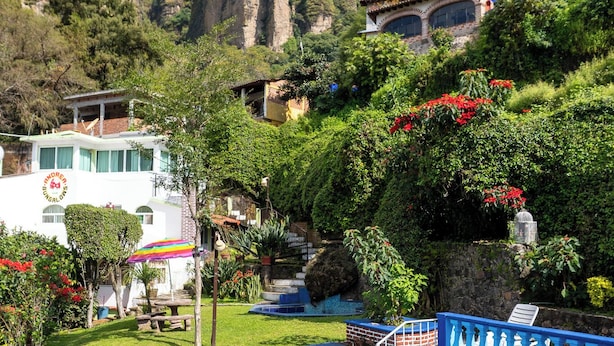 Una piscina con una decoración azul y blanca, rodeada de abundante vegetación y montañas al fondo.