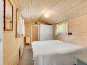 A wooden cabin bedroom with a double bed, a dresser, a mirror, a door, and a window with curtains. - "Wanna" - 600m from the sea by Interhome (Dannemare)