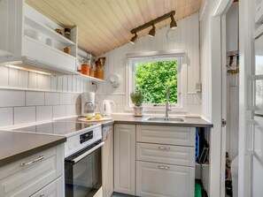 A modern kitchen with white cabinetry, a built-in oven, a coffee maker, and a window with a view of greenery. - "Wanna" - 600m from the sea by Interhome (Dannemare)