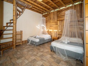 Una habitación con dos camas, cada una con mosquitero, suelo de madera, una escalera de madera y una pared de madera rústica.