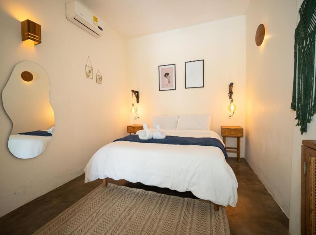 Un dormitorio con cama, lámparas de noche, aire acondicionado instalado en la pared, cuadros enmarcados y una alfombra tejida.