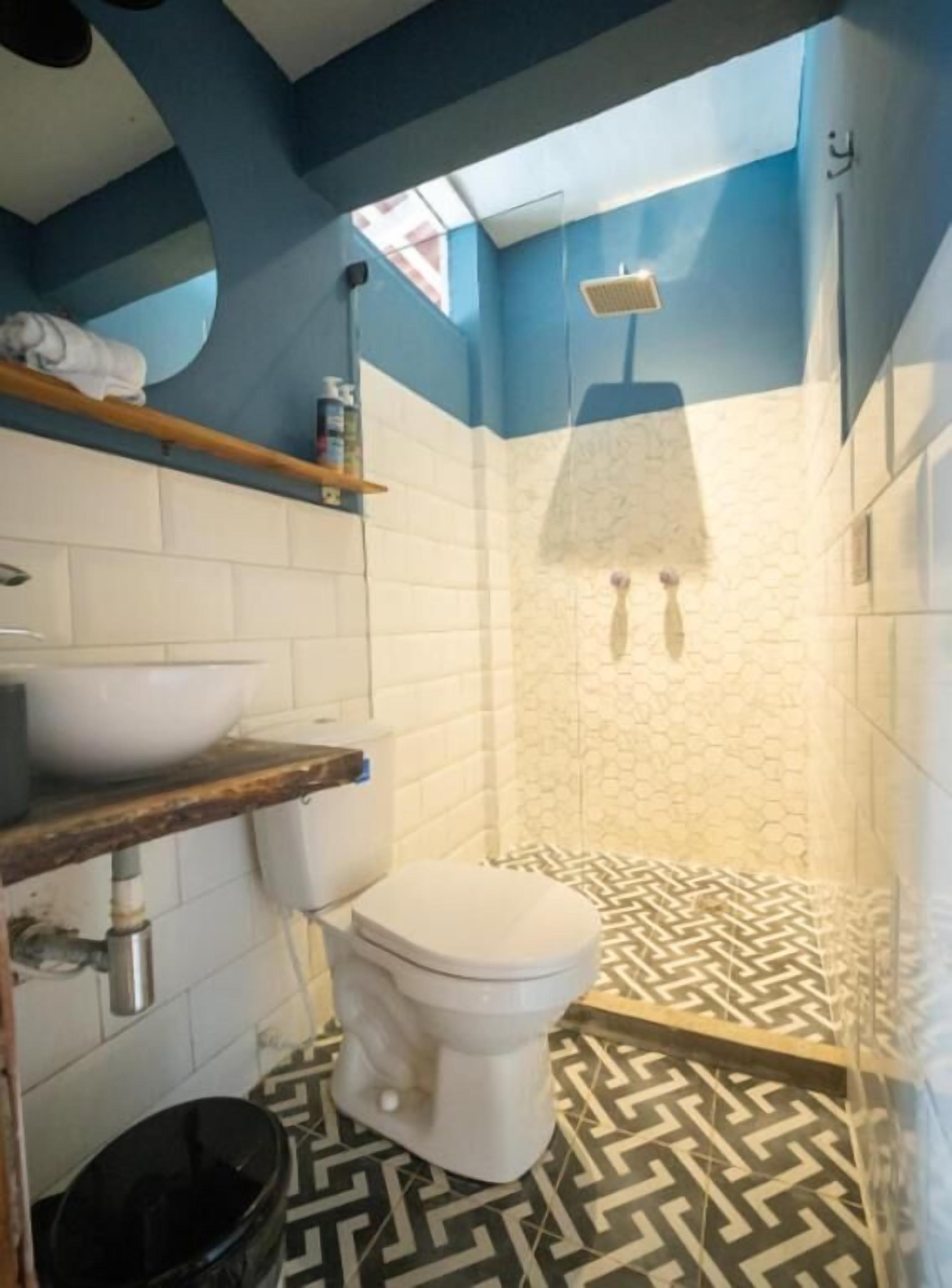 A bathroom with a white toilet, a sink, a shower, and a patterned floor.