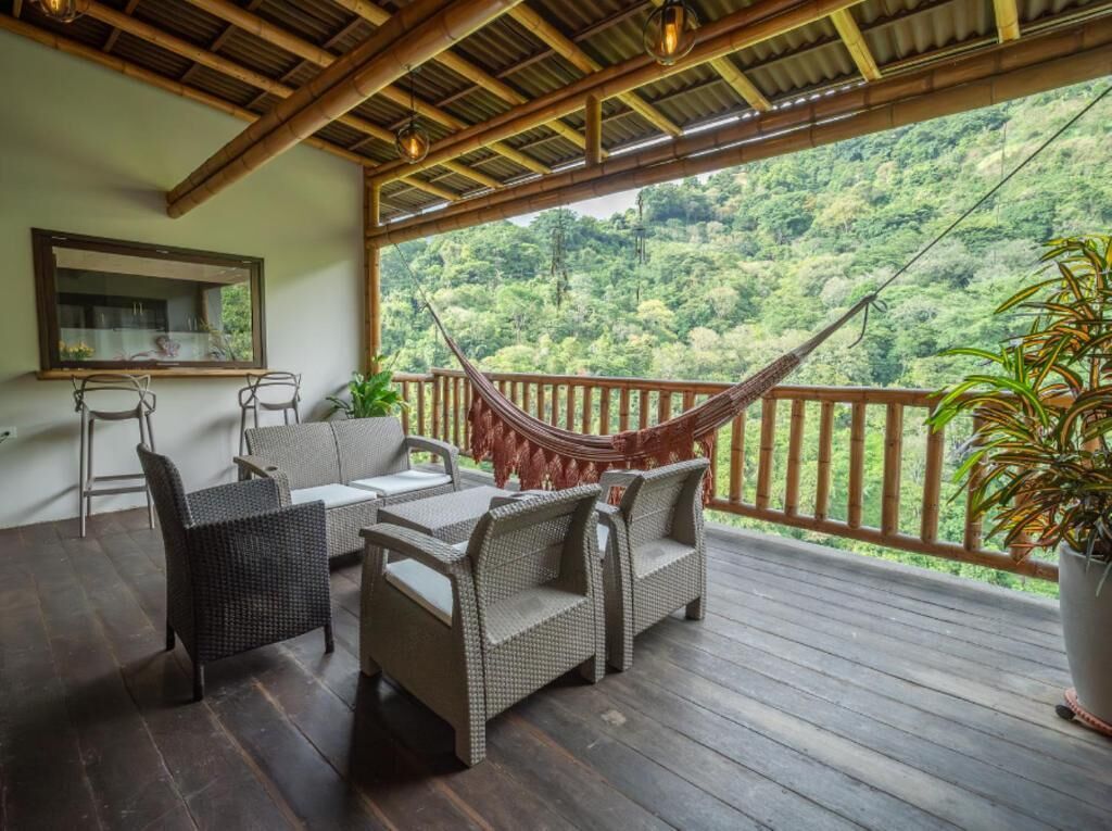 A wooden deck with wicker furniture, a hammock, and a view of a lush green hillside.