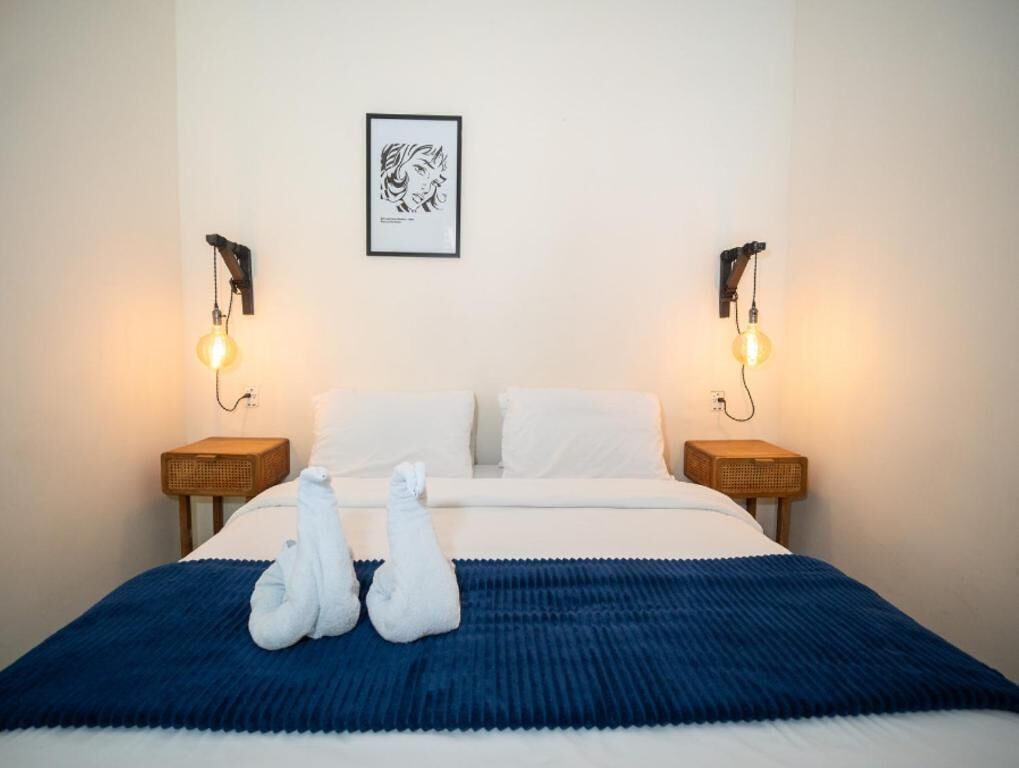 Habitación de hotel con una cama, dos lámparas de noche, una obra de arte enmarcada en la pared y una toalla sobre la cama.