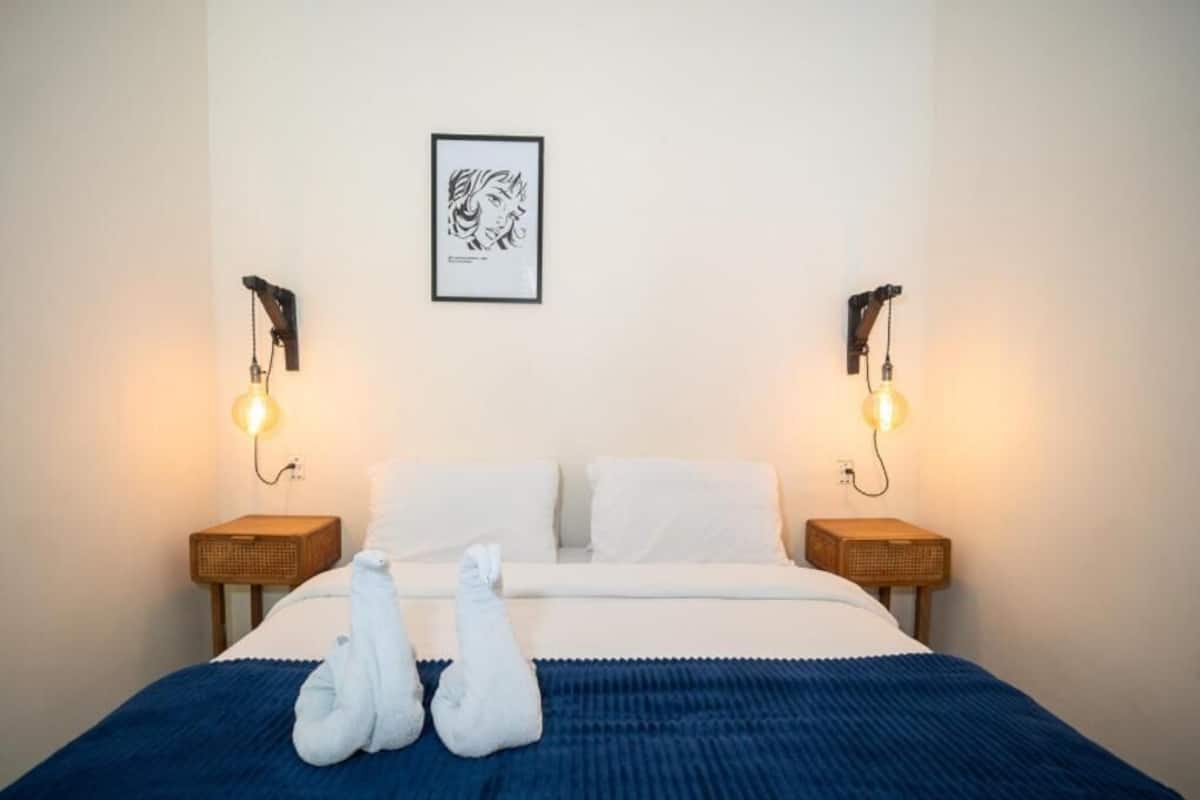 Una habitació d'hotel amb un llit, dues làmpades de nit, una obra d'art emmarcada a la paret i una tovallola sobre el llit.