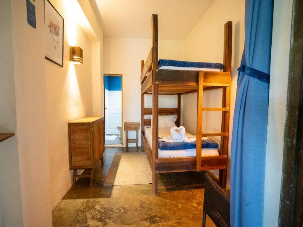 Una habitación con literas, una silla de mimbre, una mesita y una lámpara fijada a la pared.
