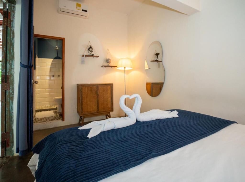 Une chambre d’hôtel avec un lit, une armoire en bois, un miroir fixé au mur et une lampe fixée au mur.