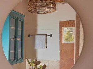 Un baño con un mueble azul, una lámpara colgante, un perchero y una ventana con vistas.