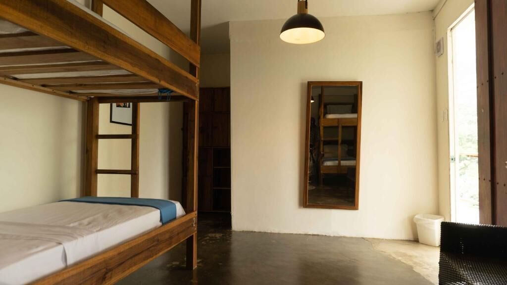 Habitación con literas, techo de madera, una cama individual, lámpara colgante y un espejo en la pared.