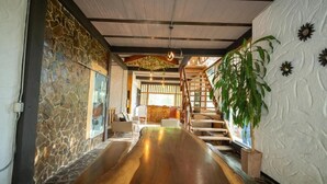 A hallway with a wooden floor, stone wall, staircase, and a potted plant.