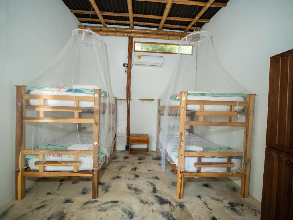 Dos camas literas de madera con mosquiteros, un taburete de madera y un armario de madera.