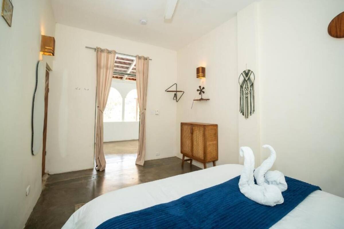 Un dormitori amb un llit, un armari de fusta, una làmpada fixa a la paret i una porta que dóna a una altra habitació.