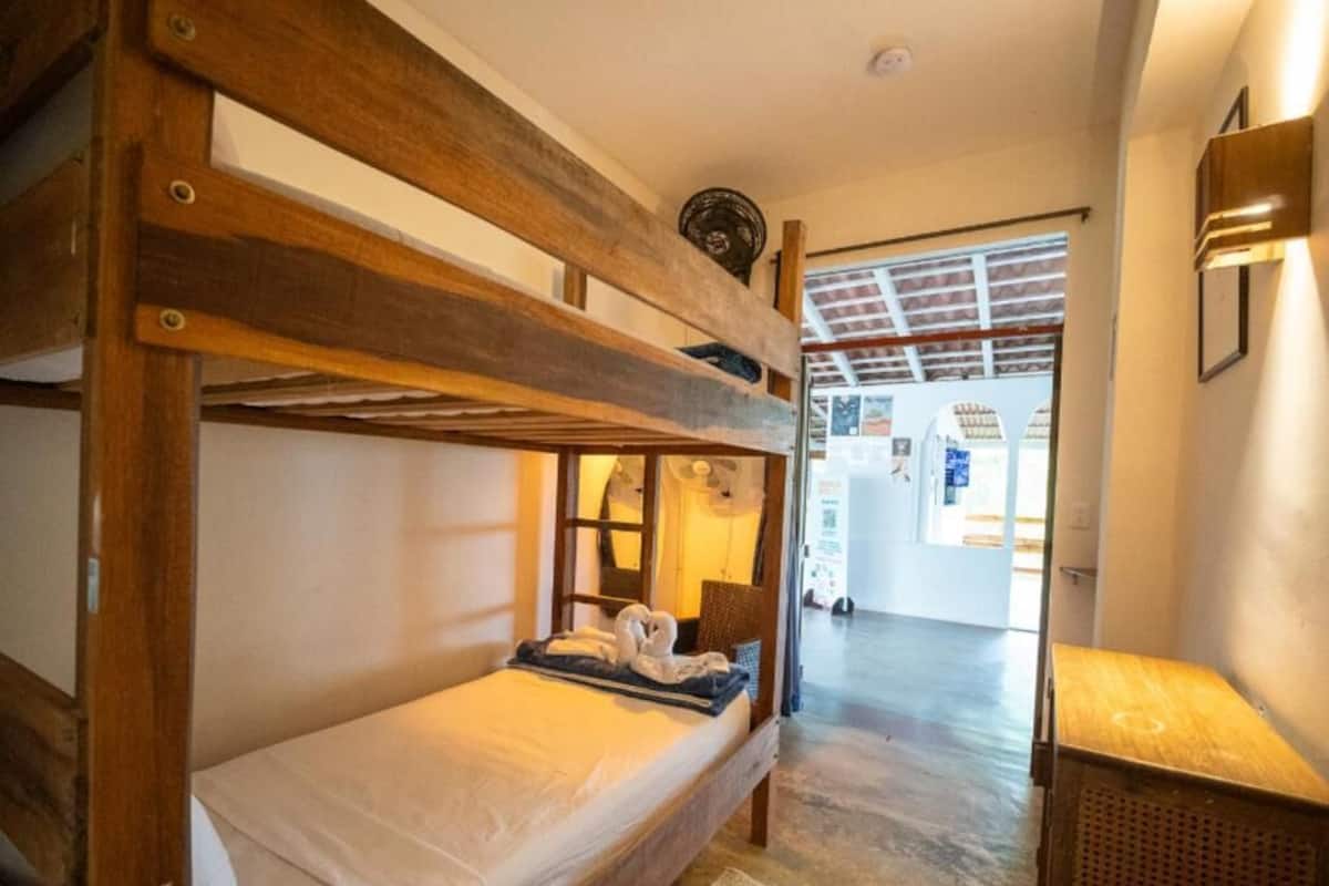 Habitació amb lliteres, un panell de fusta al capçal, una taula petita i una làmpada.
