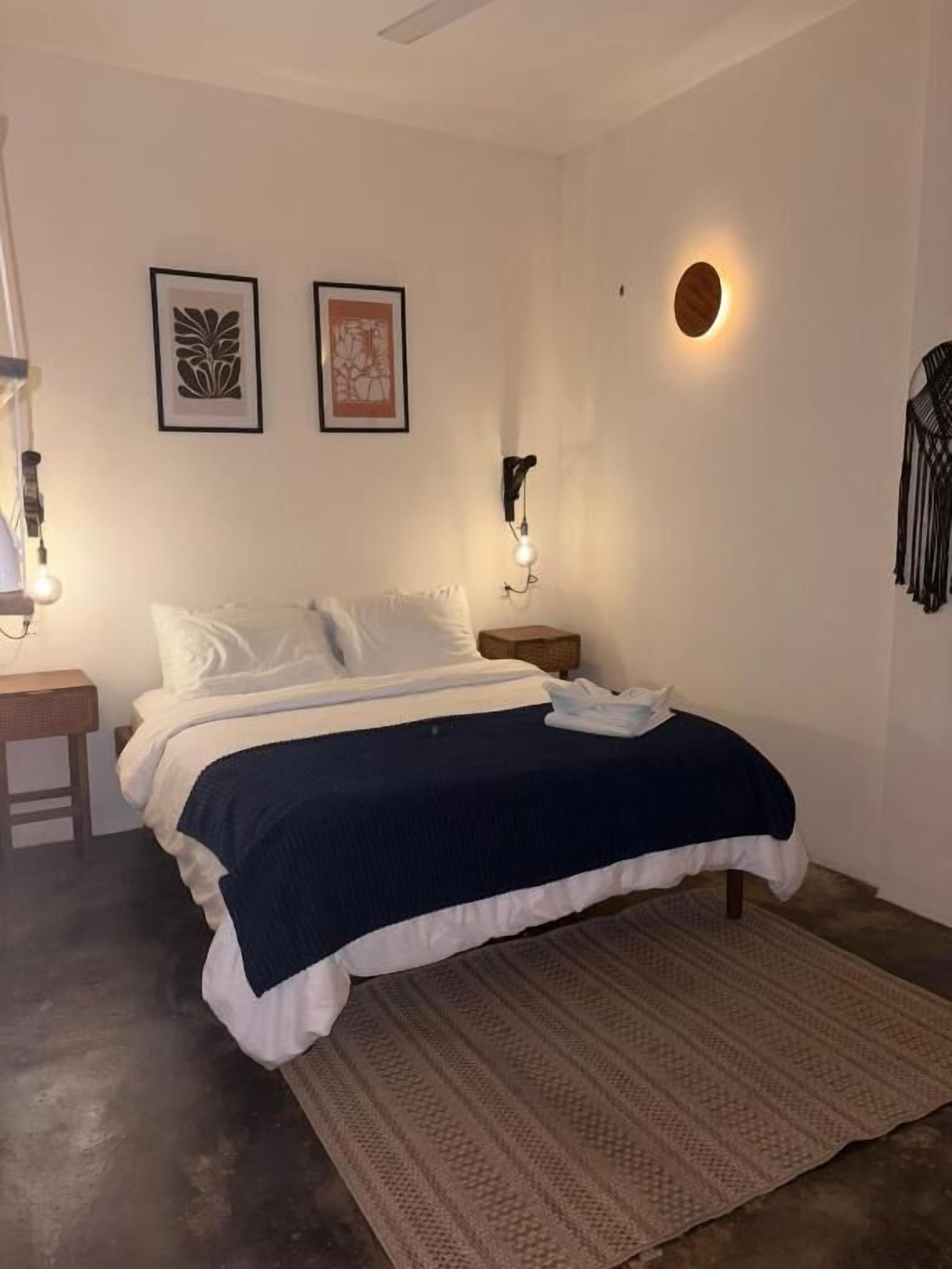 Una camera da letto con un letto, un comodino, una lampada a parete e due quadri appesi.
