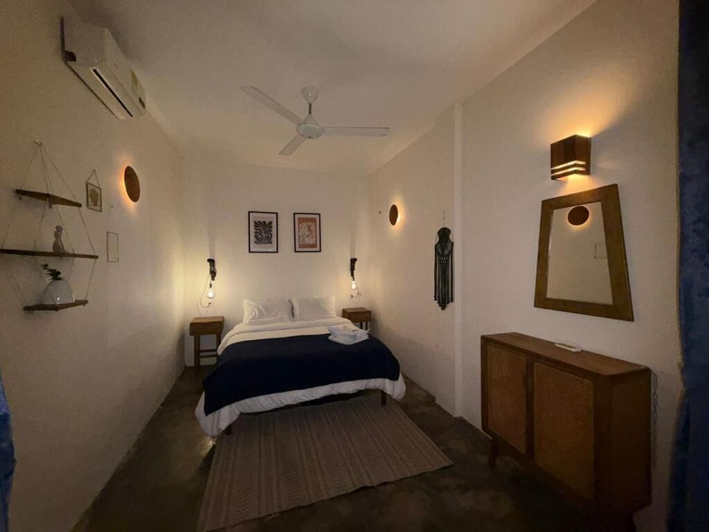 Un dormitorio con cama, mesitas de noche, ventilador de techo, luces empotradas en la pared y un espejo.