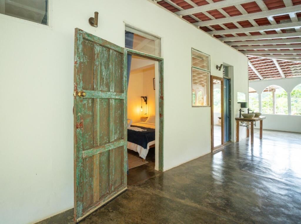 Una habitación con cama, una mesa con un cuenco y una puerta que da a otra estancia.