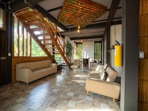 A spacious living area with a wooden staircase, a sofa, a chair, and a table. - La Veranda & Restaurant  (Minca)