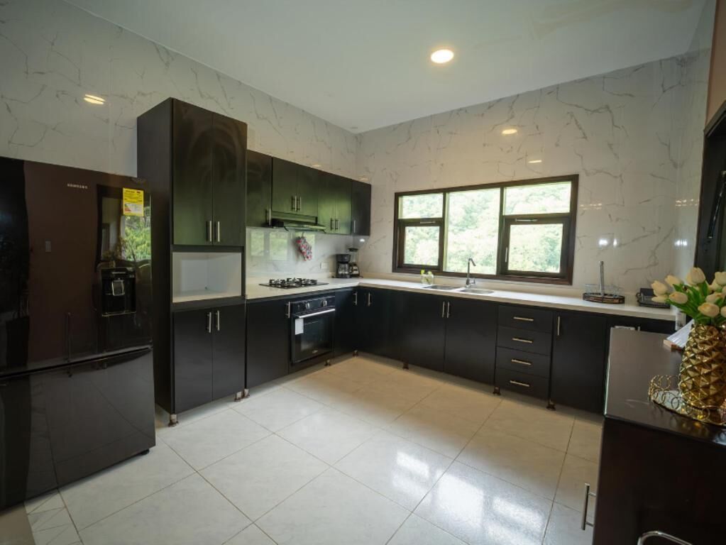 A modern kitchen with dark cabinets, a stainless steel refrigerator, and a window providing natural light.