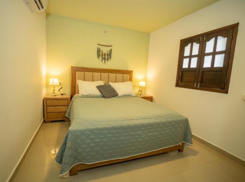 Un dormitorio con cama, mesitas de noche, una obra de arte en la pared y una ventana con vidrio esmerilado.