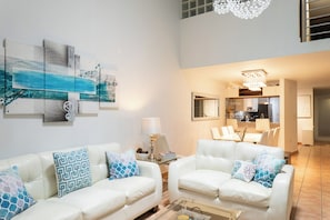 A modern living room with two white leather sofas, a coffee table, and a dining area with a chandelier. - Oceanside Golf and Resort Villa in Dorado (Dorado)