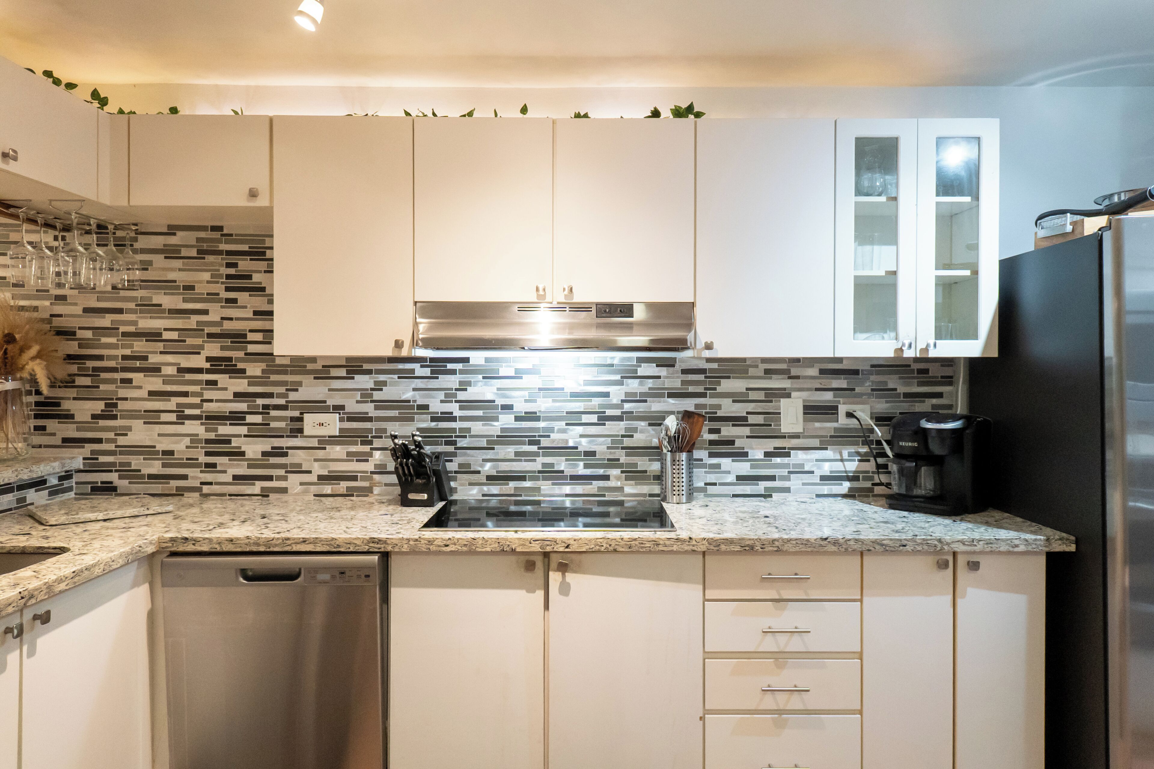 Una cocina moderna con armarios blancos, una campana extractora de acero inoxidable, un refrigerador negro y un salpicadero de azulejos.