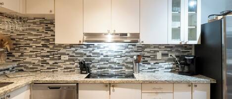 Una cocina moderna con armarios blancos, una campana extractora de acero inoxidable, un refrigerador negro y un salpicadero de azulejos.